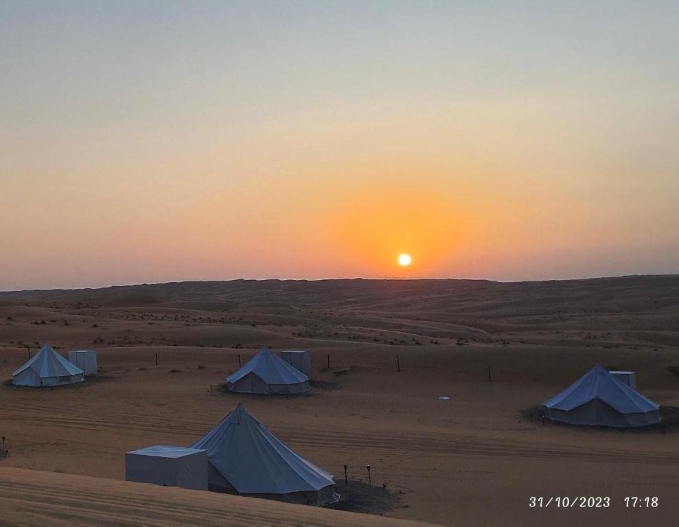 BadīyahDesert Stars Camp的日落时分在沙漠中的一组帐篷