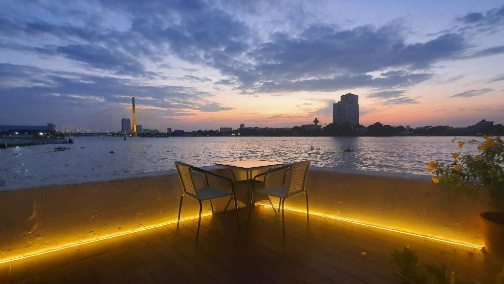 曼谷Riverfront house/Chao phraya river/Baan Rimphraya的一张桌子和两把椅子坐在水边的甲板上