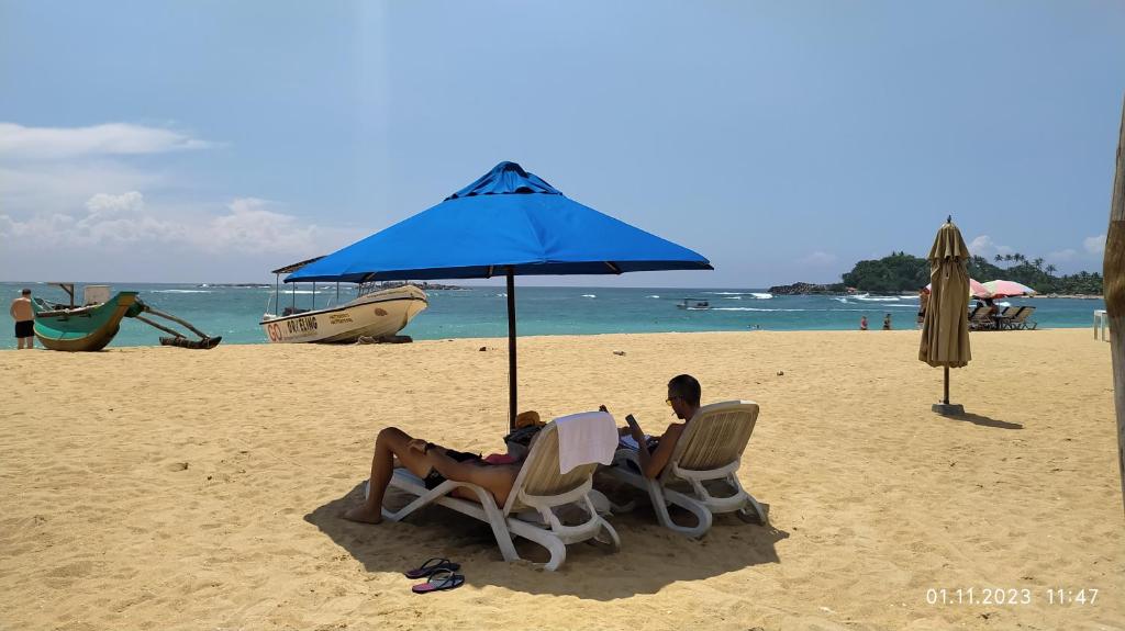 乌纳瓦图纳Full Moon Resort的两人坐在海滩上一把遮阳伞下的椅子上