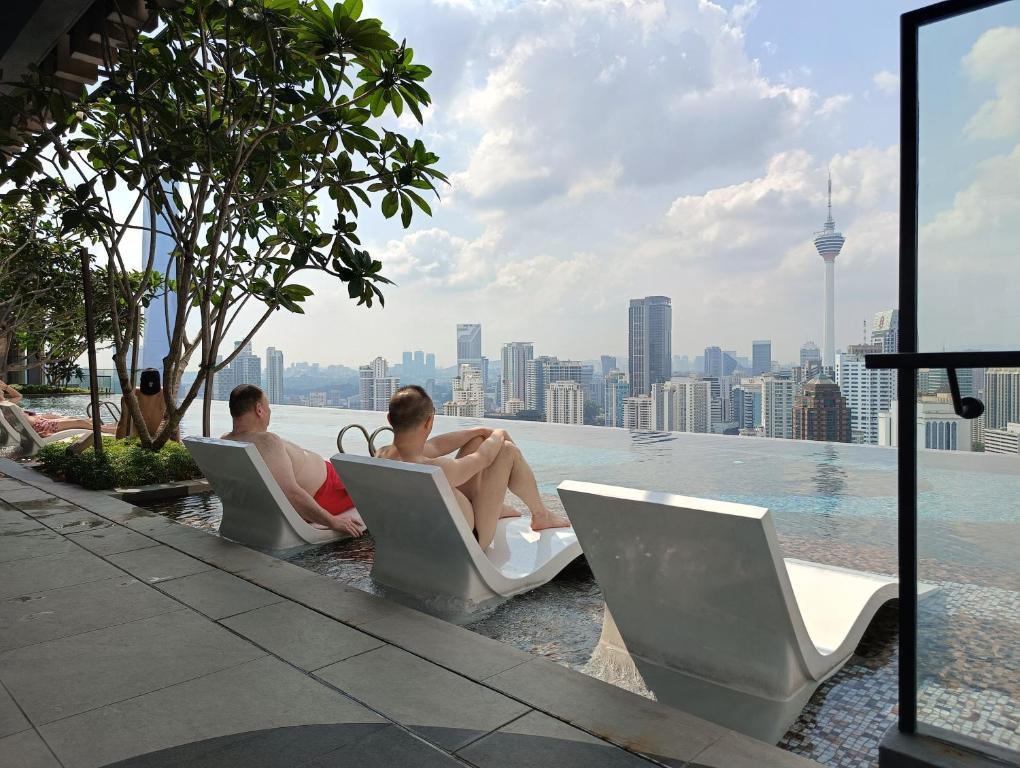 吉隆坡KLCC Suites At Axon Residence的两人坐在游泳池边的椅子上