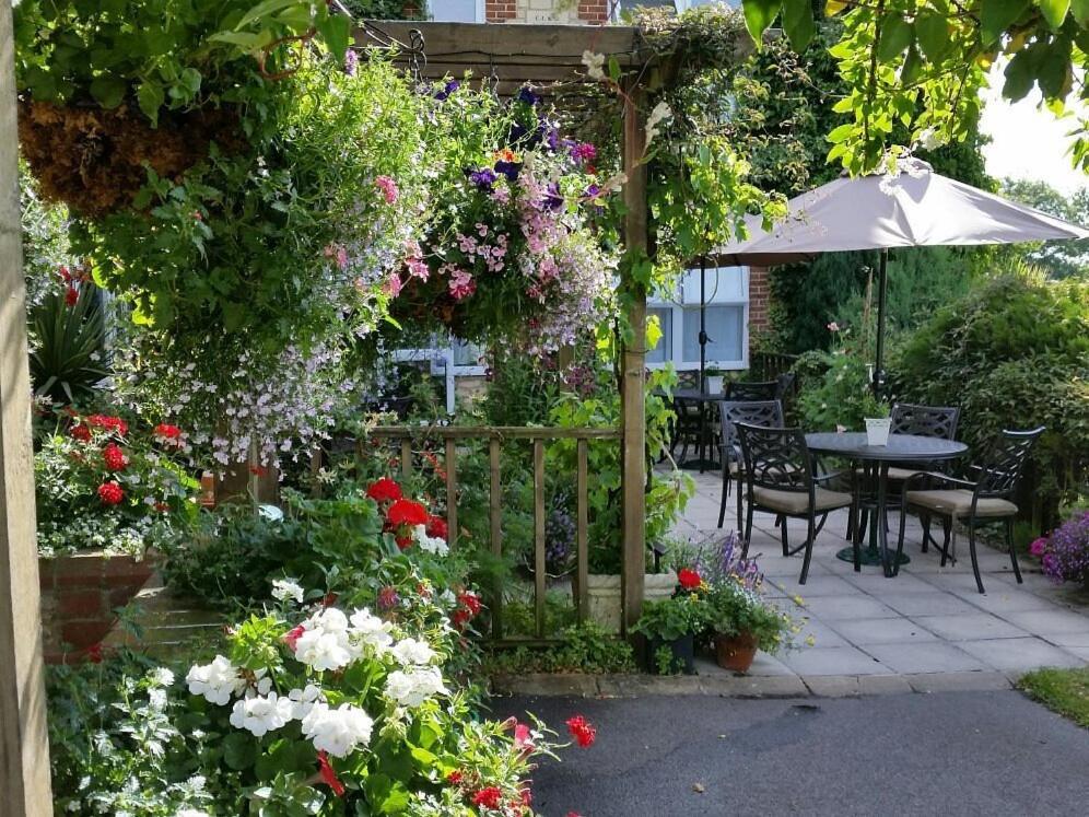 史云顿Bolingbroke Arms & Hotel的花园种有鲜花,设有桌子和雨伞