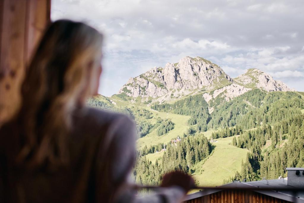 索内纳尔佩·纳斯费尔德Almresort Sonnenalpe by ALPS RESORTS的一位女人看着窗外的山地