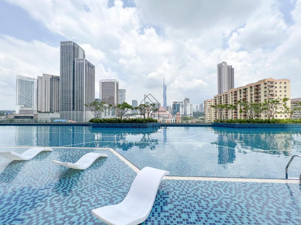 吉隆坡Sentral Suites at Kuala Lumpur Sentral by Veedu Hauz的一个带两把椅子的游泳池,享有城市天际线