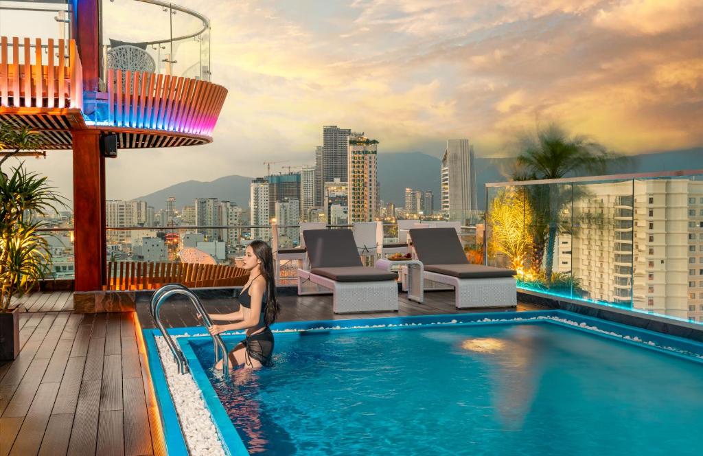 岘港Mercy Emerald Hotel的坐在建筑物顶部游泳池里的女人