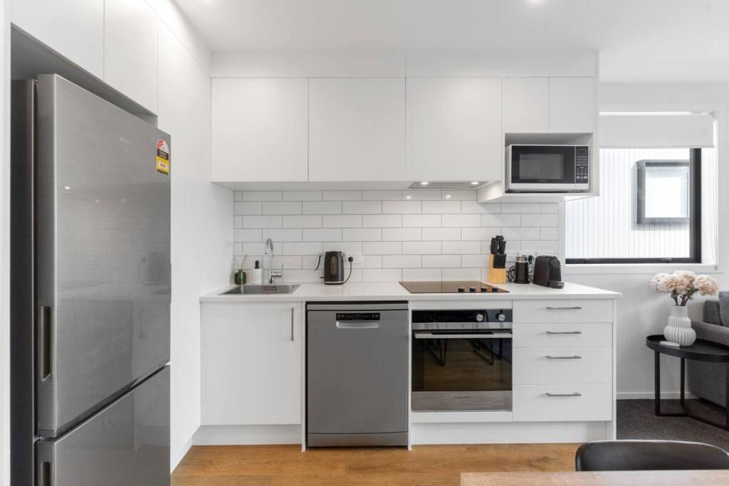 奥克兰Contemporary Urban Retreat的厨房配有白色橱柜和不锈钢冰箱
