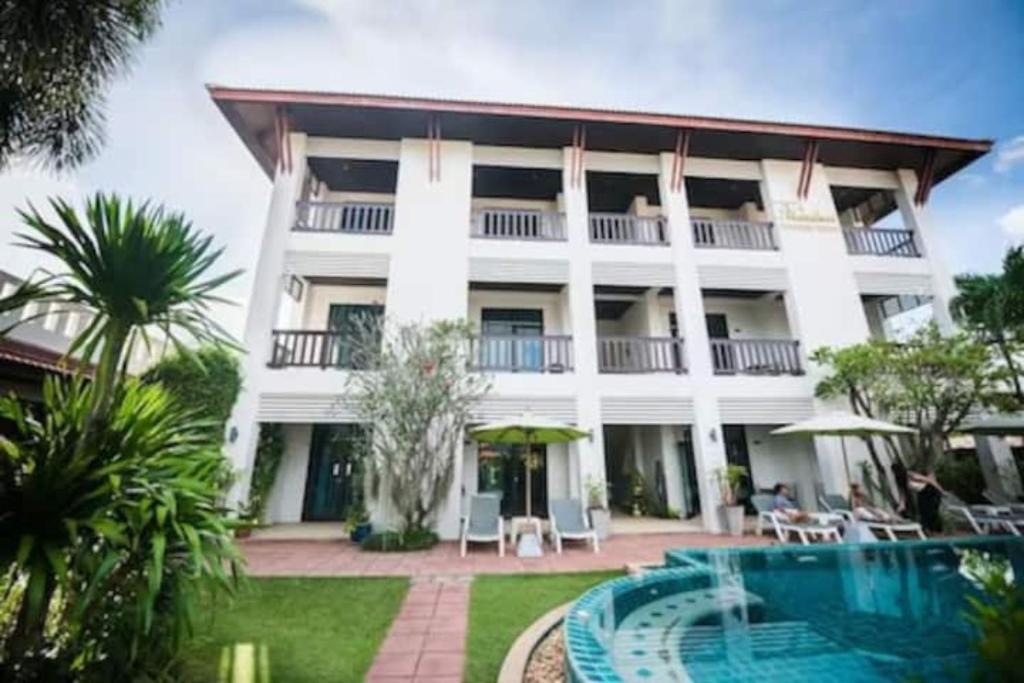 拉威海滩Monaburi Boutique Resort的一座白色的大建筑,前面设有一个游泳池