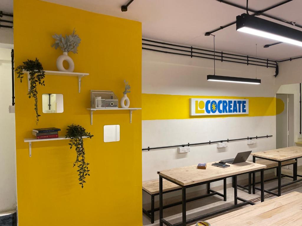 孟买Locomo Express - Stay Work Eat的办公室里黄色的墙壁,有两张桌子和一台笔记本电脑