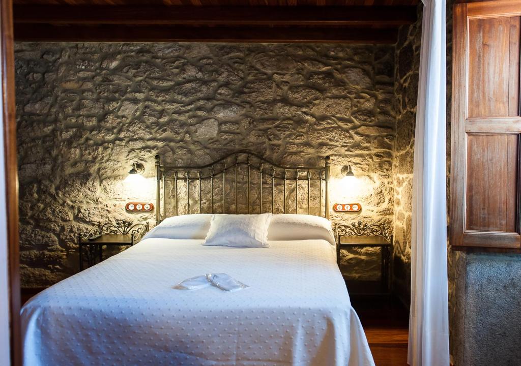 圣地亚哥－德孔波斯特拉Casa de Costoia的卧室配有一张白色大床和石墙