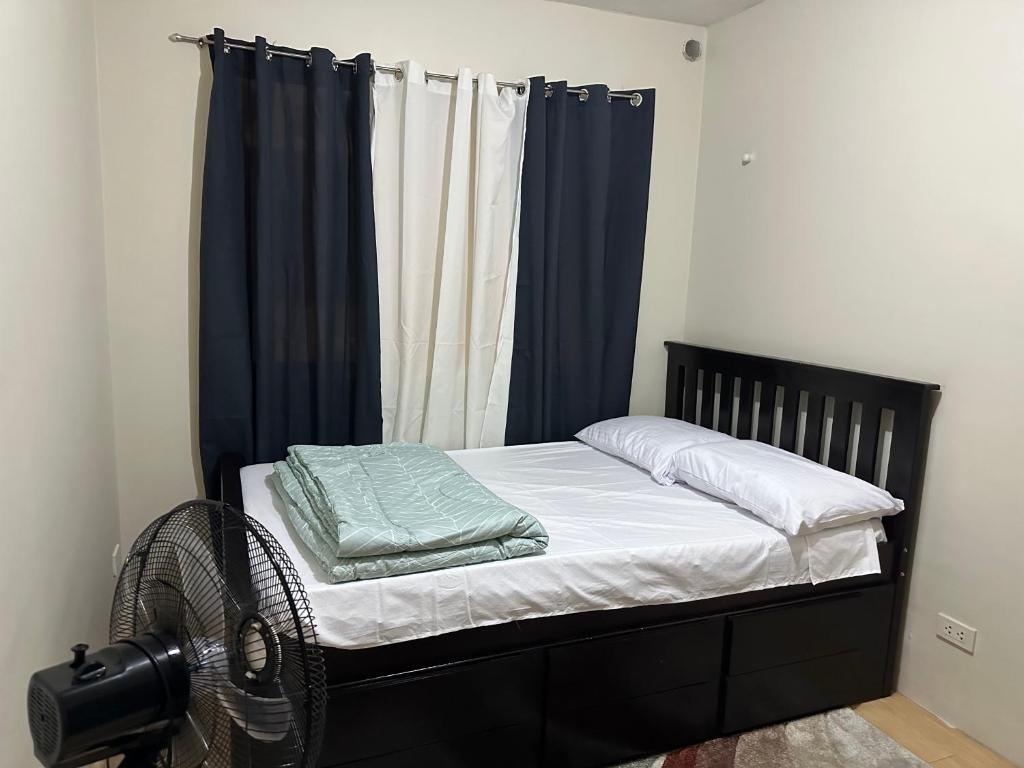 马尼拉Sorrento Oasis 2 BR的一间卧室配有一张带蓝色窗帘的床和风扇