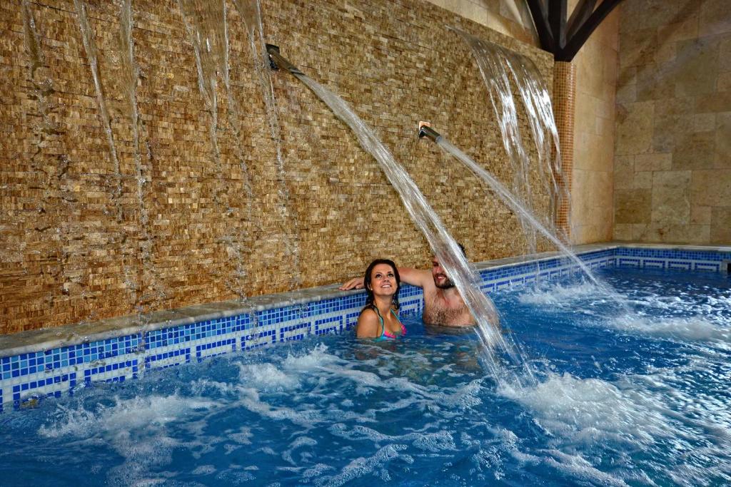 苏普拉希尔Hotel Supraśl的两个女人在一个带瀑布的游泳池里