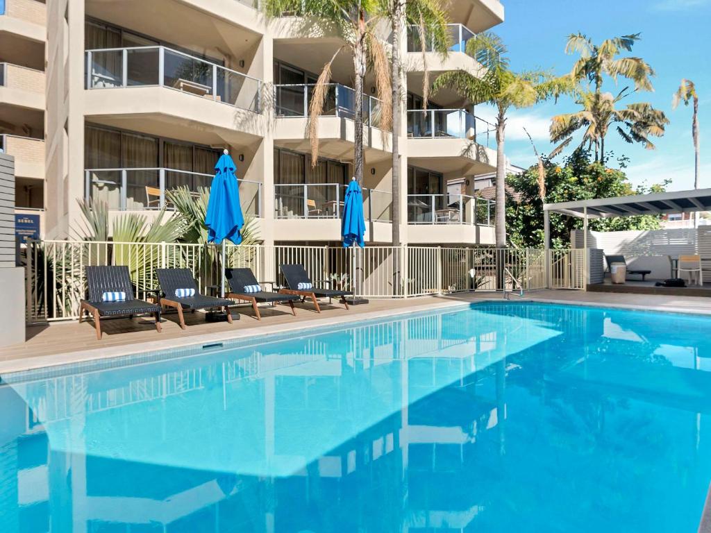 悉尼悉尼曼利海滩塞贝尔酒店的大楼前的游泳池配有椅子和遮阳伞