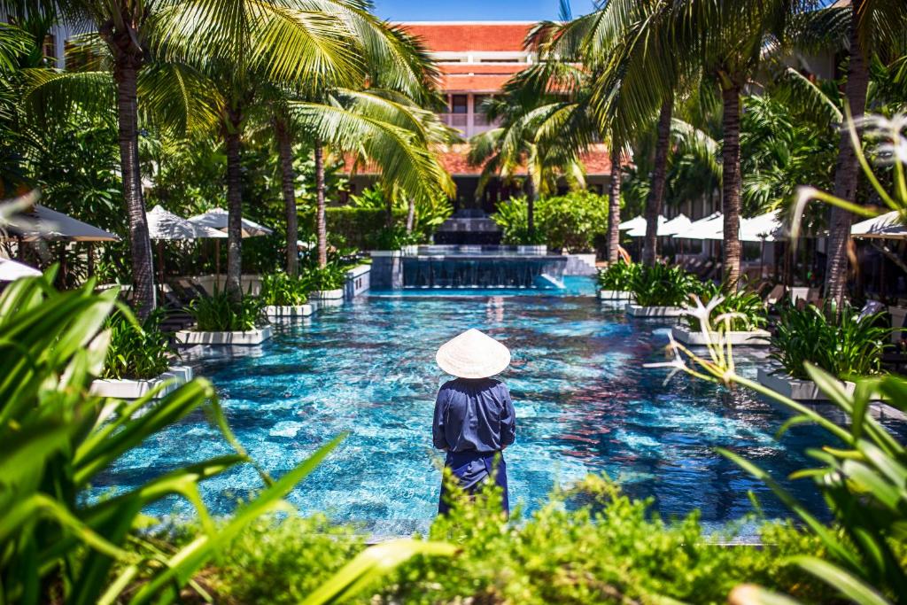 会安Almanity Hoi An Resort & Spa的戴帽子的人站在泳池前