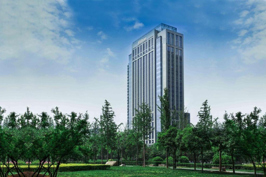 西安Hilton Xi'an High-tech Zone的一座高大的建筑,在公园里,有树木