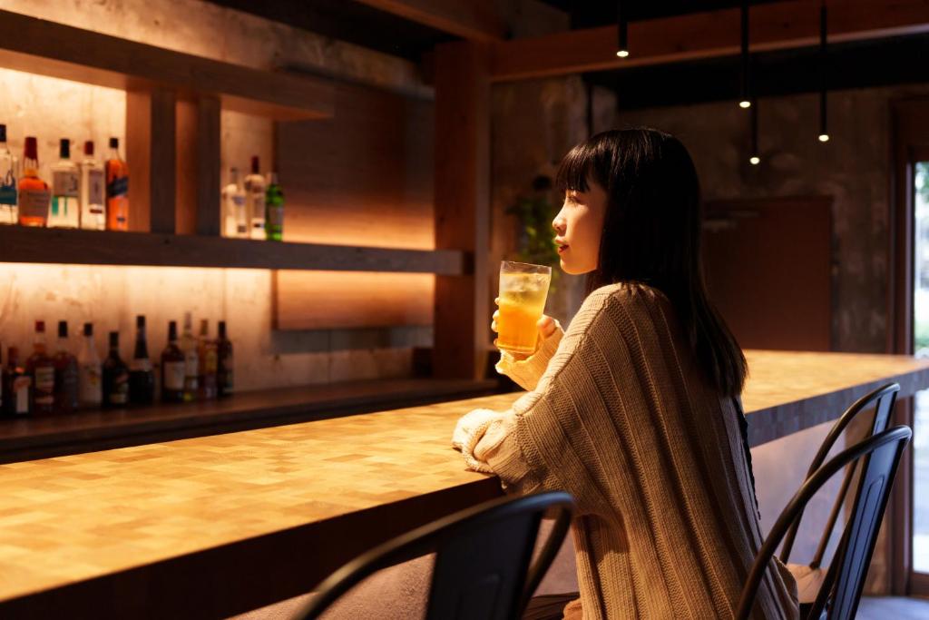 大阪3U NAMBA MINAMI by DOYANEN的坐在酒吧里拿着玻璃的女人