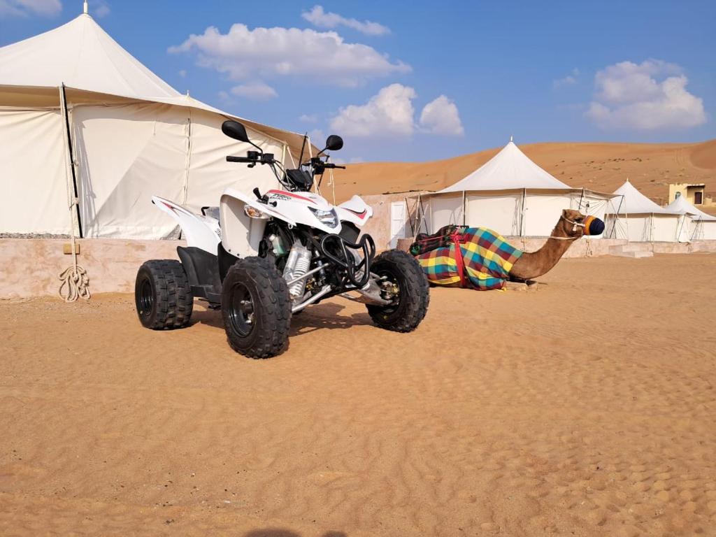 BadīyahAl Salam Desert Camp Bidiya的一辆四轮车停在沙漠中,有帐篷