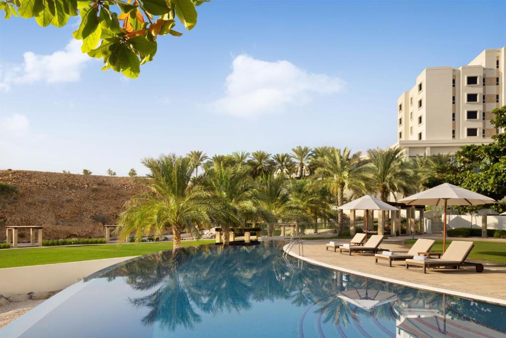 马斯喀特JW Marriott Hotel Muscat的一个带椅子和棕榈树的度假村游泳池