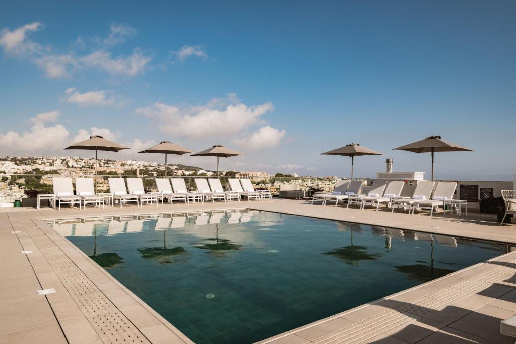 圣朱利安斯AC Hotel by Marriott St Julian's的屋顶上带椅子和遮阳伞的游泳池