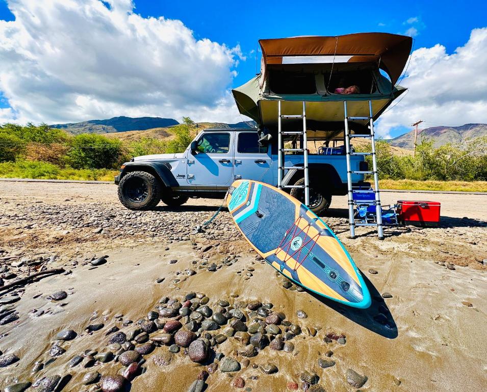 帕依亚Explore Maui's diverse campgrounds and uncover the island's beauty from fresh perspectives every day as you journey with Aloha Glamp's great jeep equipped with a rooftop tent的坐在海滩上的冲浪板,旁边一辆卡车