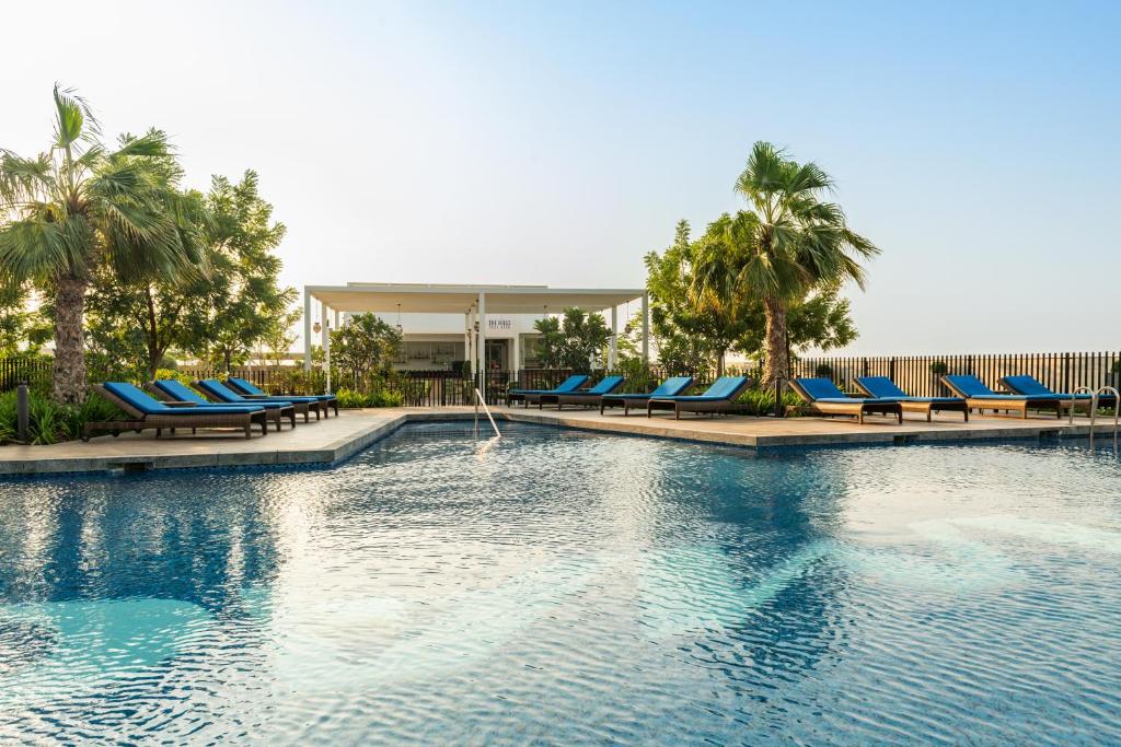 迪拜Radisson Dubai Damac Hills的一个带蓝色躺椅的游泳池,棕榈树