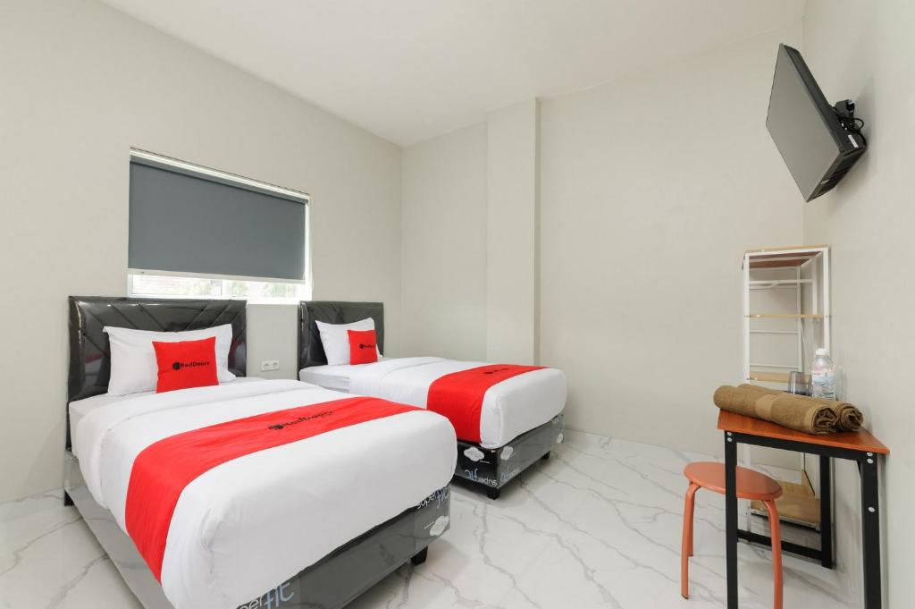HajimanaRedDoorz near GSG UNILA Lampung的白色客房的两张床,配有红色枕头