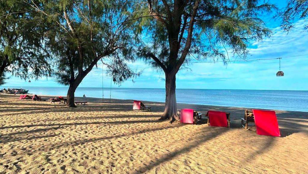 Sathing Phra敖泰度假酒店的海滩上,有红椅子和树木,还有大海