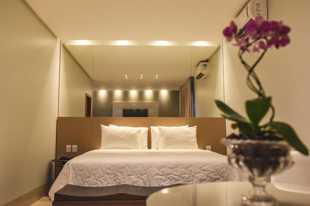 古鲁皮Hotel D'Leon的一间卧室,配有一张床和一个花瓶,桌子上放着鲜花