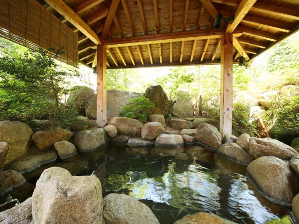 大町市梦之汤酒店的一个带岩石和木屋顶的池塘