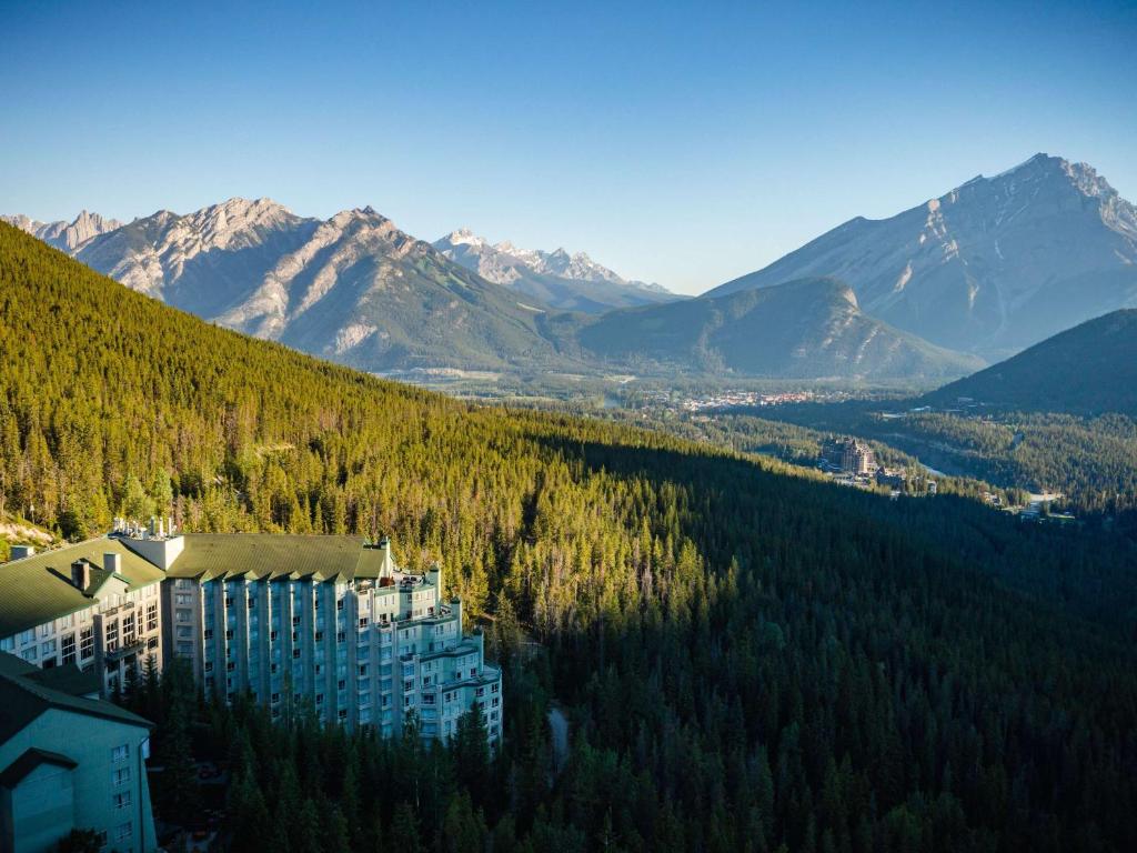 班夫The Rimrock Resort Hotel Banff的一座拥有树木和山脉的山丘建筑
