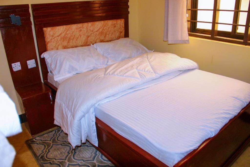 NjombeGetaway bnb - Njombe的一张铺有白色床单的床和木制床头板