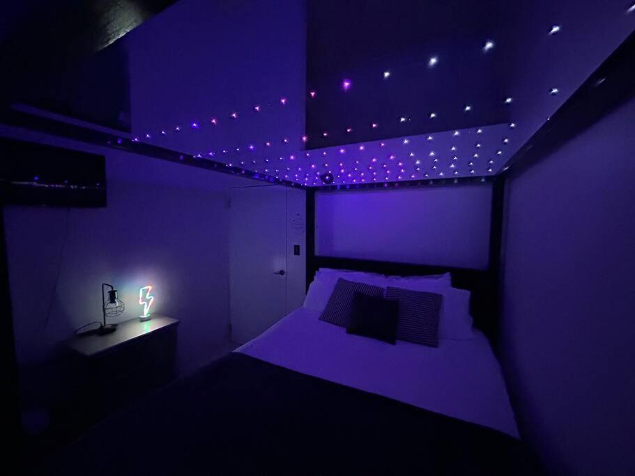 瓜亚马City Dreams Cozy Loft in Guayama Great Location的紫色卧室配有一张床和一张带台灯的桌子