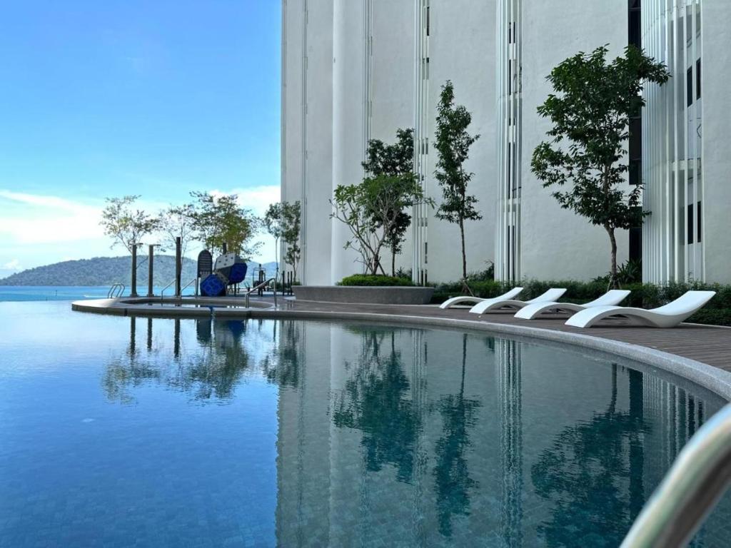 哥打京那巴鲁The Shore Kota Kinabalu by Ariana的一座带白色椅子的游泳池,位于大楼旁