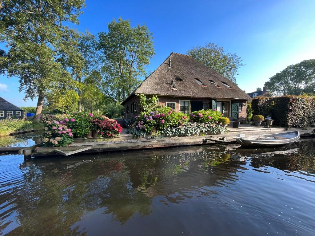 羊角村Plompeblad Suite Giethoorn的茅草屋顶和水面花草的房子