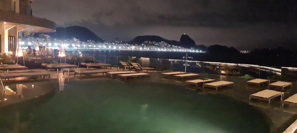 里约热内卢COPACABANA,LEME,AV ATLÂNTICA, FRENTE PARA O MAR!!!的夜间带桌椅的游泳池