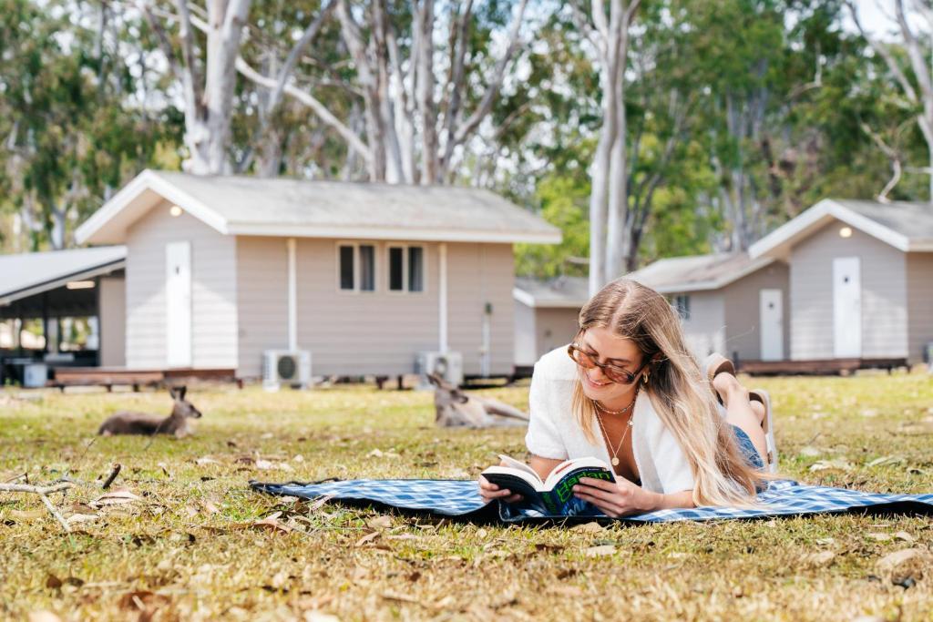 CootharabaKangaROOMS Noosa Everglades YHA的躺在草地上读书的女人