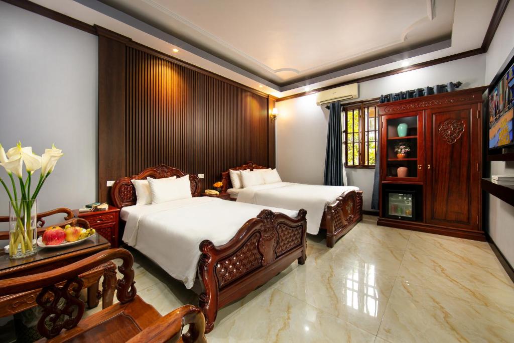 河内Nam Hai Hotel的一间卧室设有两张床和一张带一碗水果的桌子。
