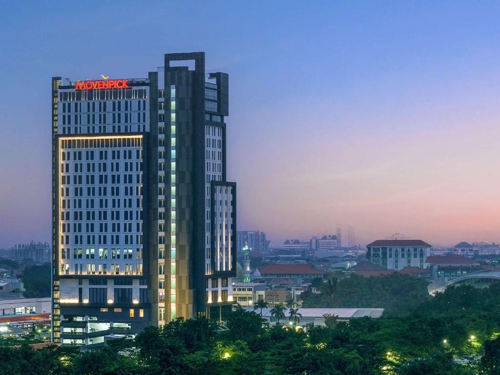 泗水Movenpick Surabaya City的一座高大的建筑,上面有 ⁇ 虹灯标志