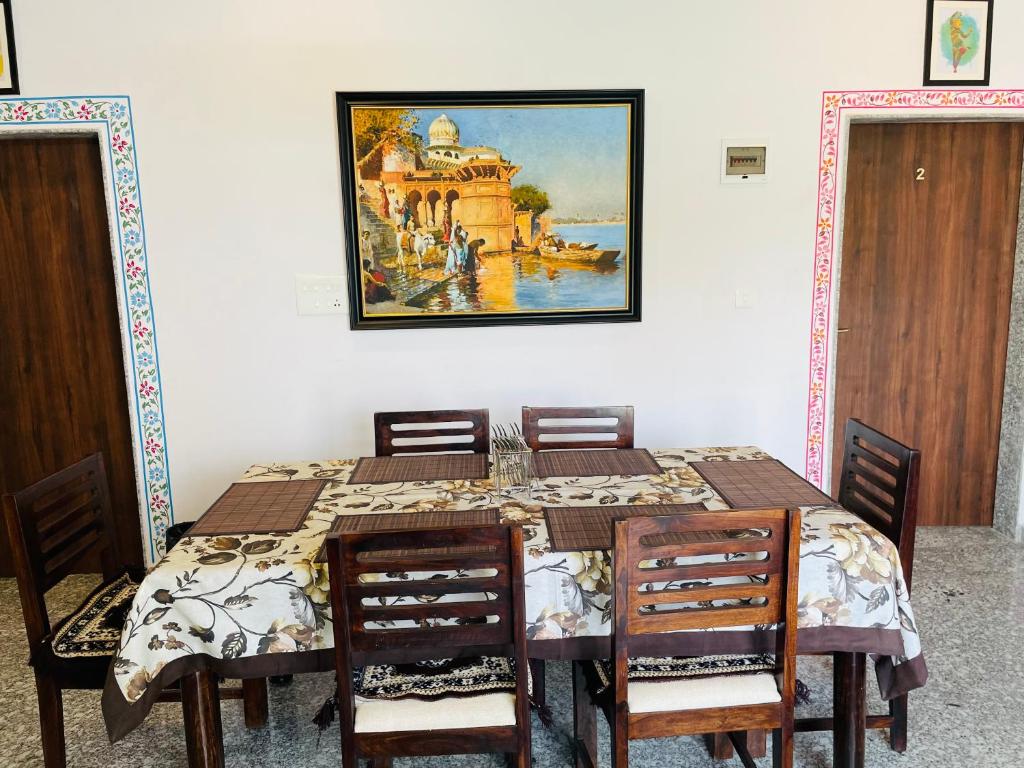 乌代浦Krishna kottage A Boutique Home Stay的餐桌、椅子和墙上的绘画