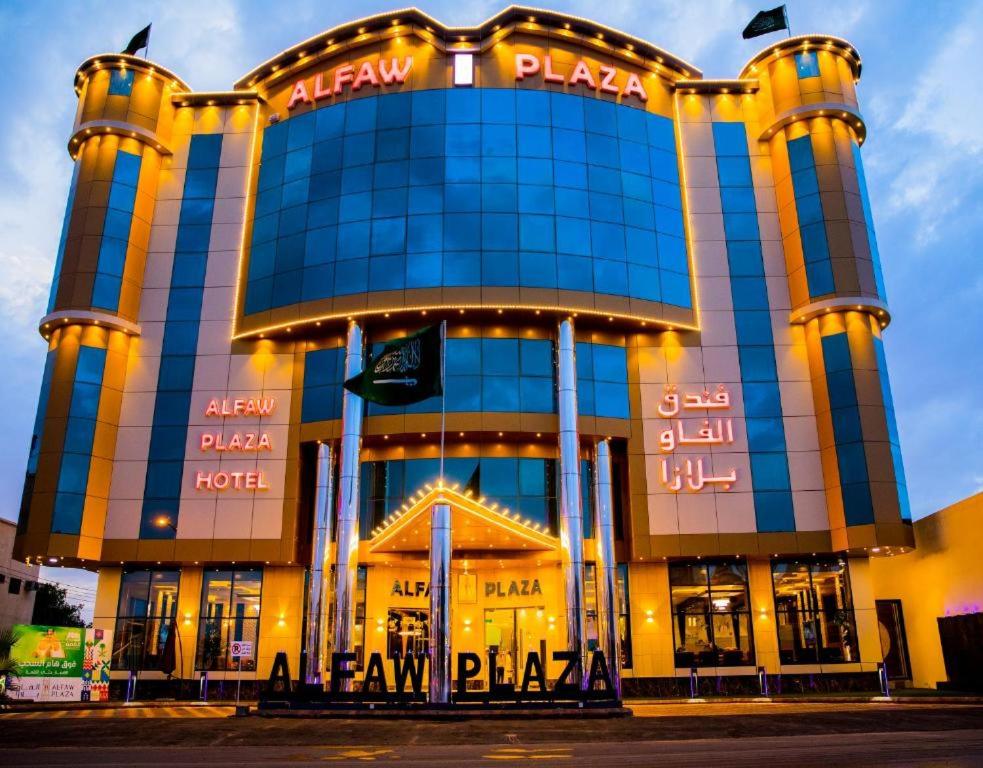 沙鲁拉HOTEL ALFAW PLAZA的前面有 ⁇ 虹灯标志的大建筑
