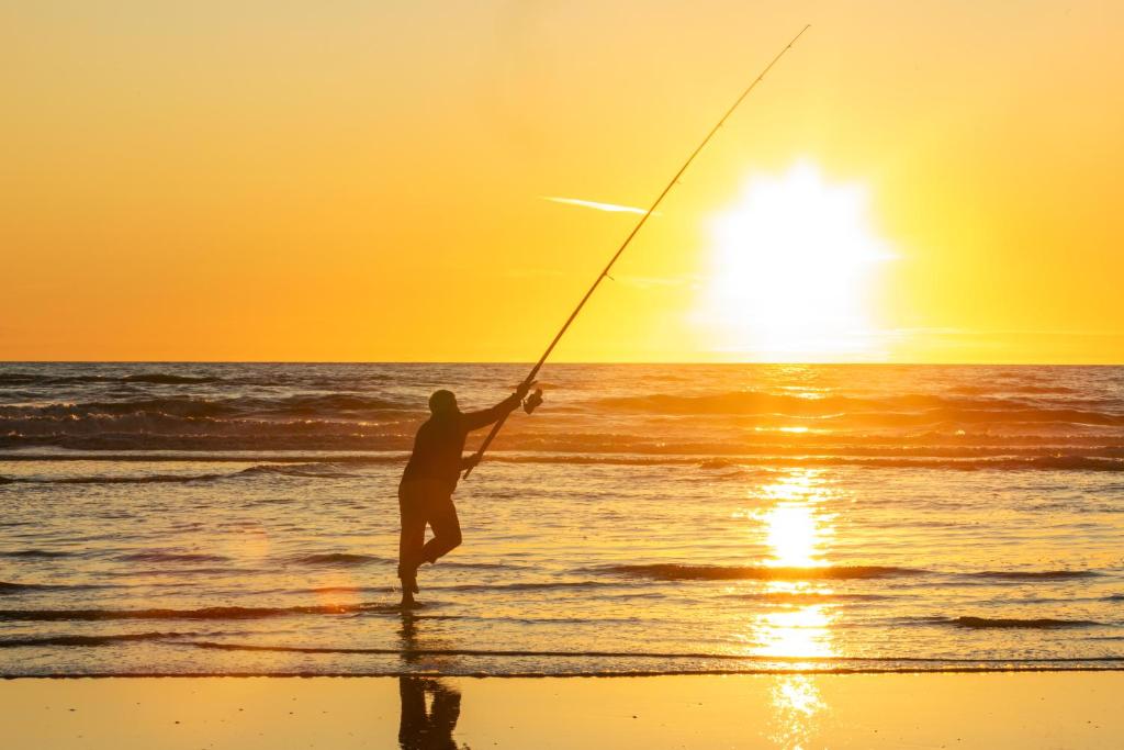 Foxton BeachFoxton Beach Holiday Park的日落时分在海滩上钓鱼的男人