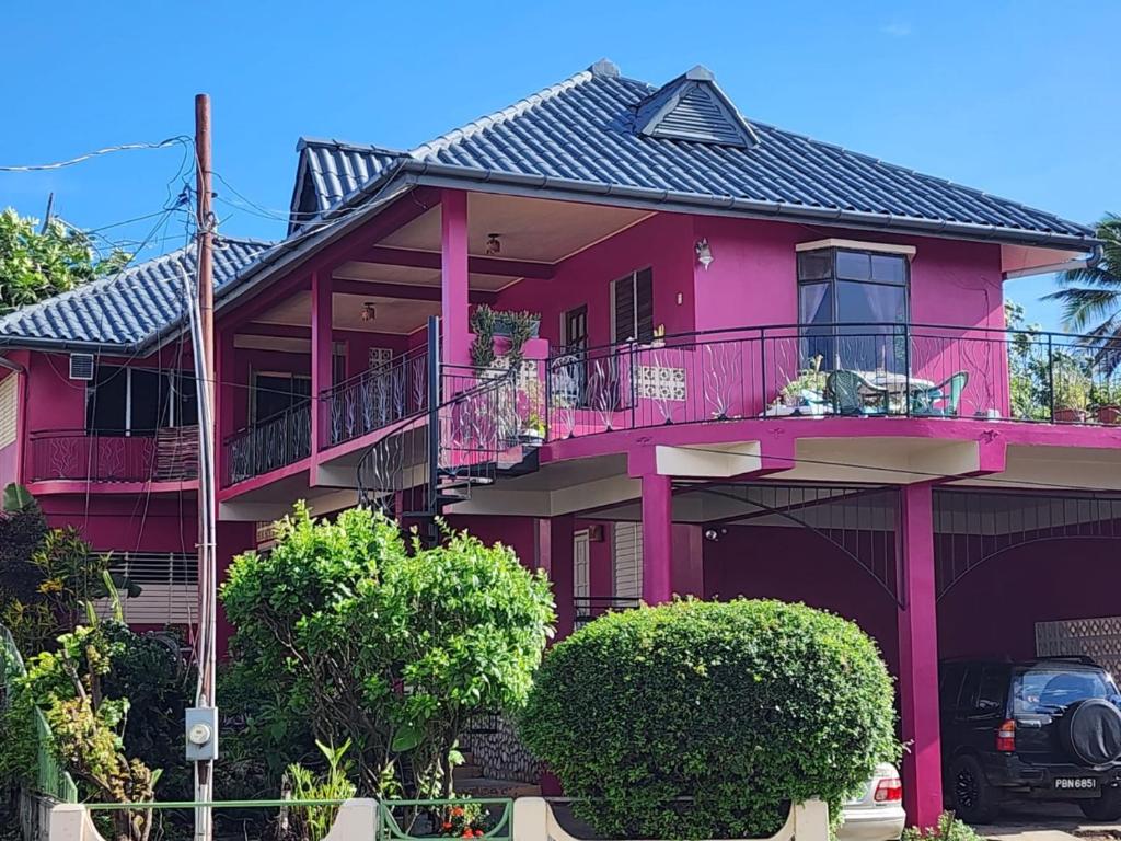 BuccooThe Seaside Garden Guesthouse的粉红色的房子设有阳台和灌木丛