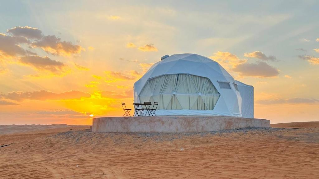 BadīyahMilky way Domes Desert Camp的沙漠中的帐篷,背景是日落