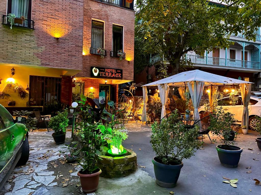 第比利斯Terrace Tbilisi Center的一座建筑前方的带植物和遮阳伞的庭院