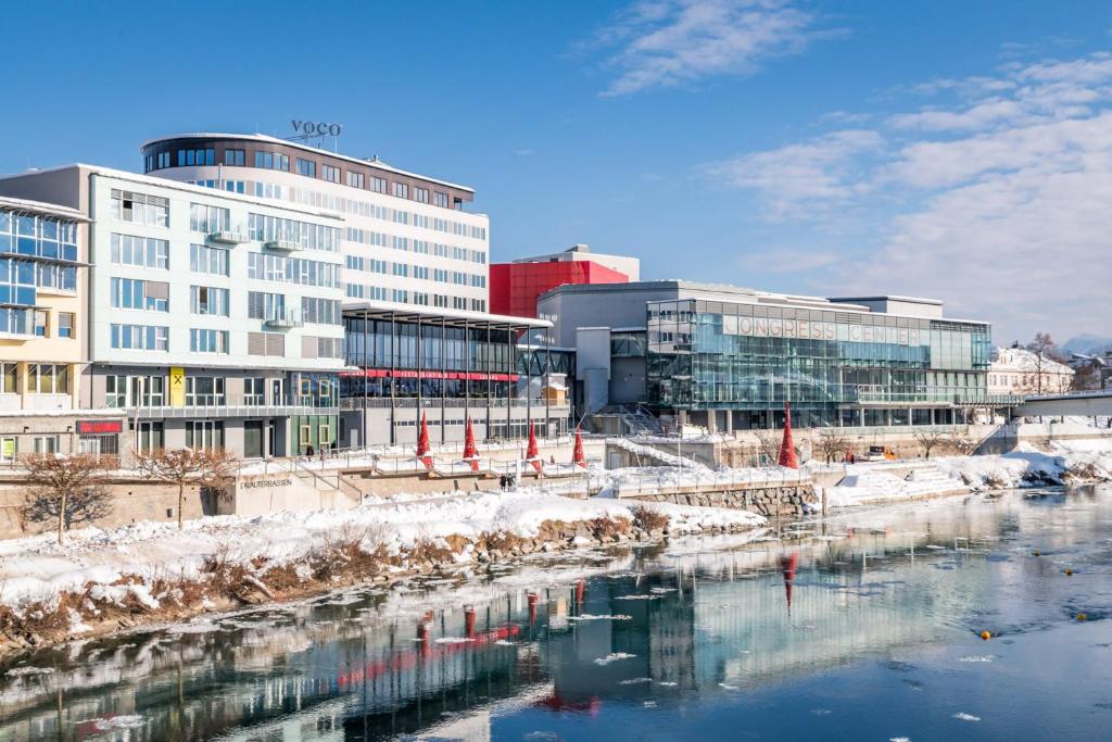 菲拉赫voco® Villach, an IHG Hotel的一座有建筑物的城市,一条有雪的河流