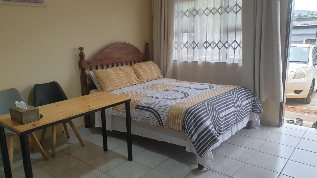 曼齐尼Manzini, Park Vills Apartment, No 103的一间卧室配有一张床、一张桌子和一个窗户。
