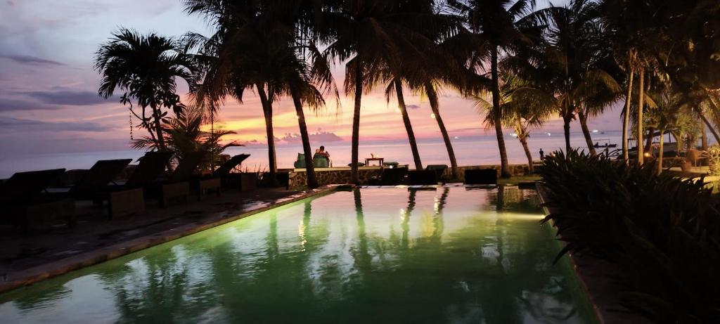 罗威那1000梦幻简易别墅酒店的棕榈树泳池和日落背景