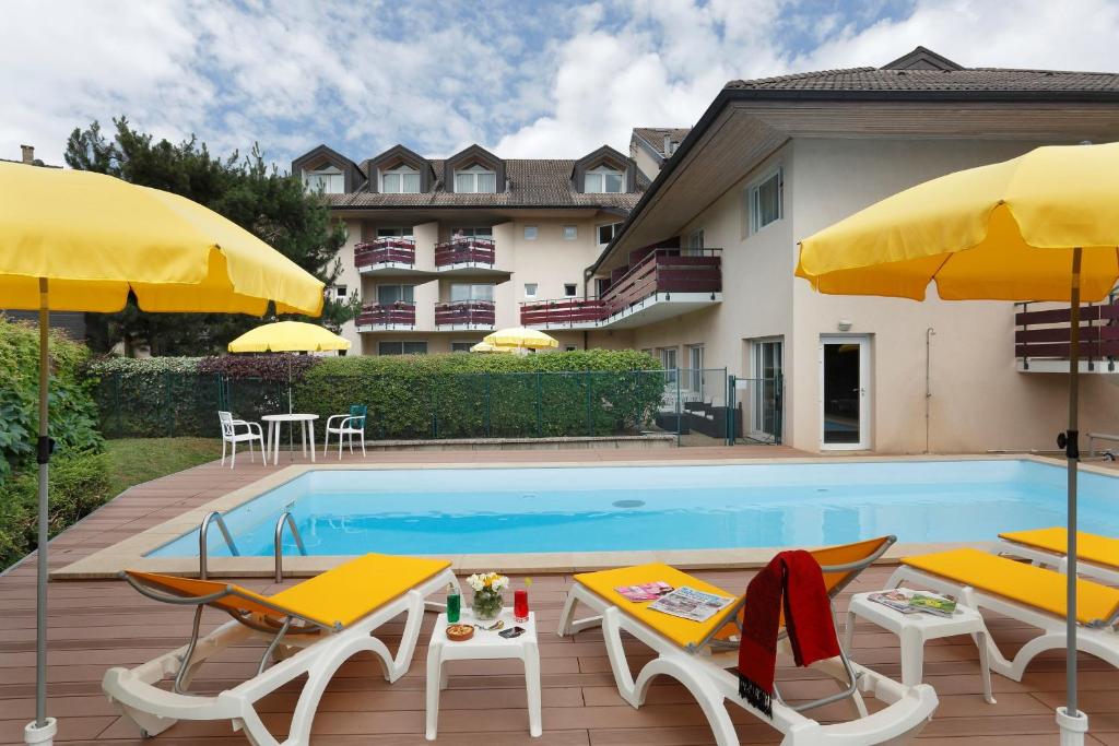 托农莱班Logis Hotel Arc En Ciel的一座带椅子和遮阳伞的游泳池位于一座建筑旁边