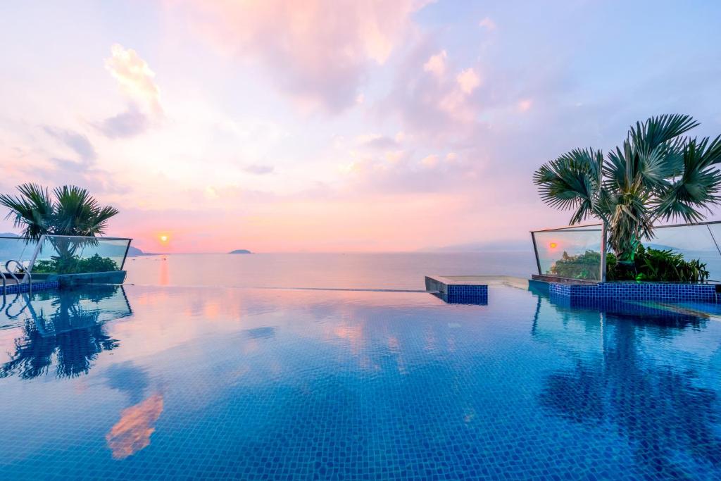 芽庄Boton Blue Hotel & Spa的日落时分棕榈树和海洋的游泳池