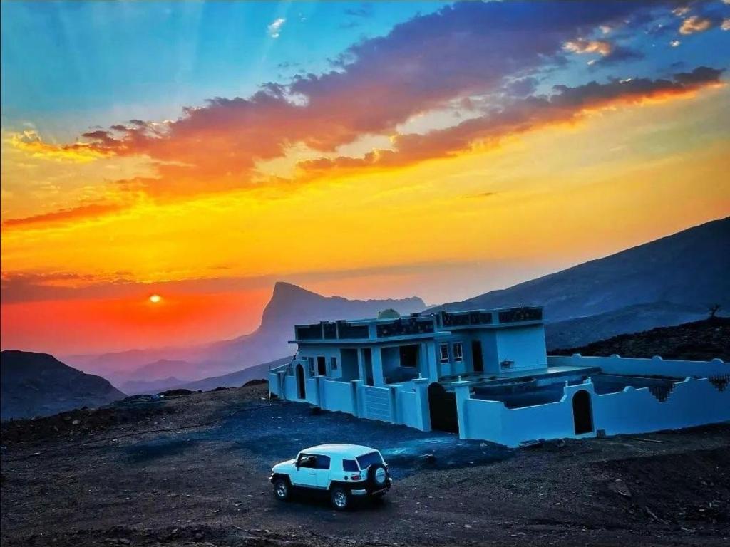 MisfāhJabal Shams bayt kawakib的白车停在建筑物前面,有日落