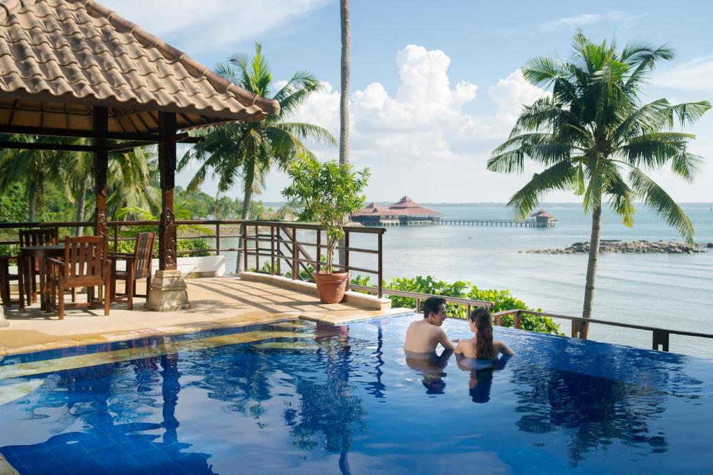 拉古洼因陀罗玛雅泳池别墅酒店的坐在游泳池俯瞰大海的男人和女人