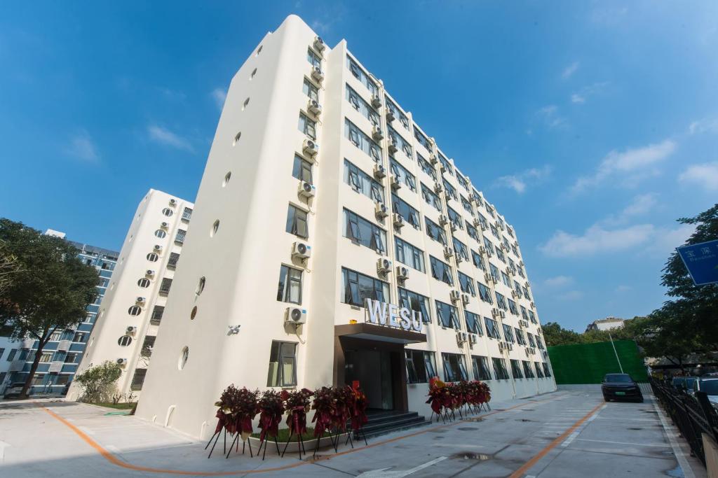 深圳WESU微宿服务公寓(深圳松坪山科技园店)的前方有红花的白色建筑